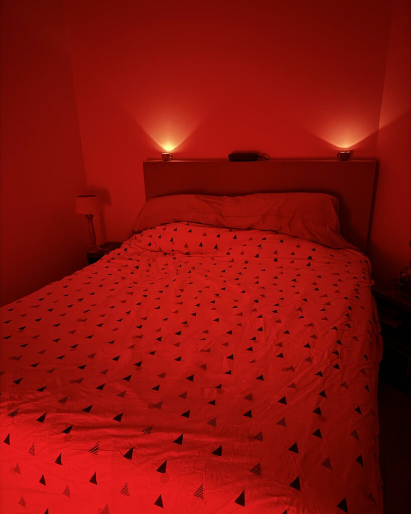 Chambre baignée d'une lumière rouge : lit double à housse à motifs triangles et deux lampes de chevet allumées.