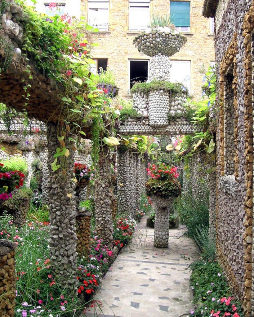 Allée du jardin Rosa Mir : colonnes et vasques de galets, foisonnement de fleurs et de verdure