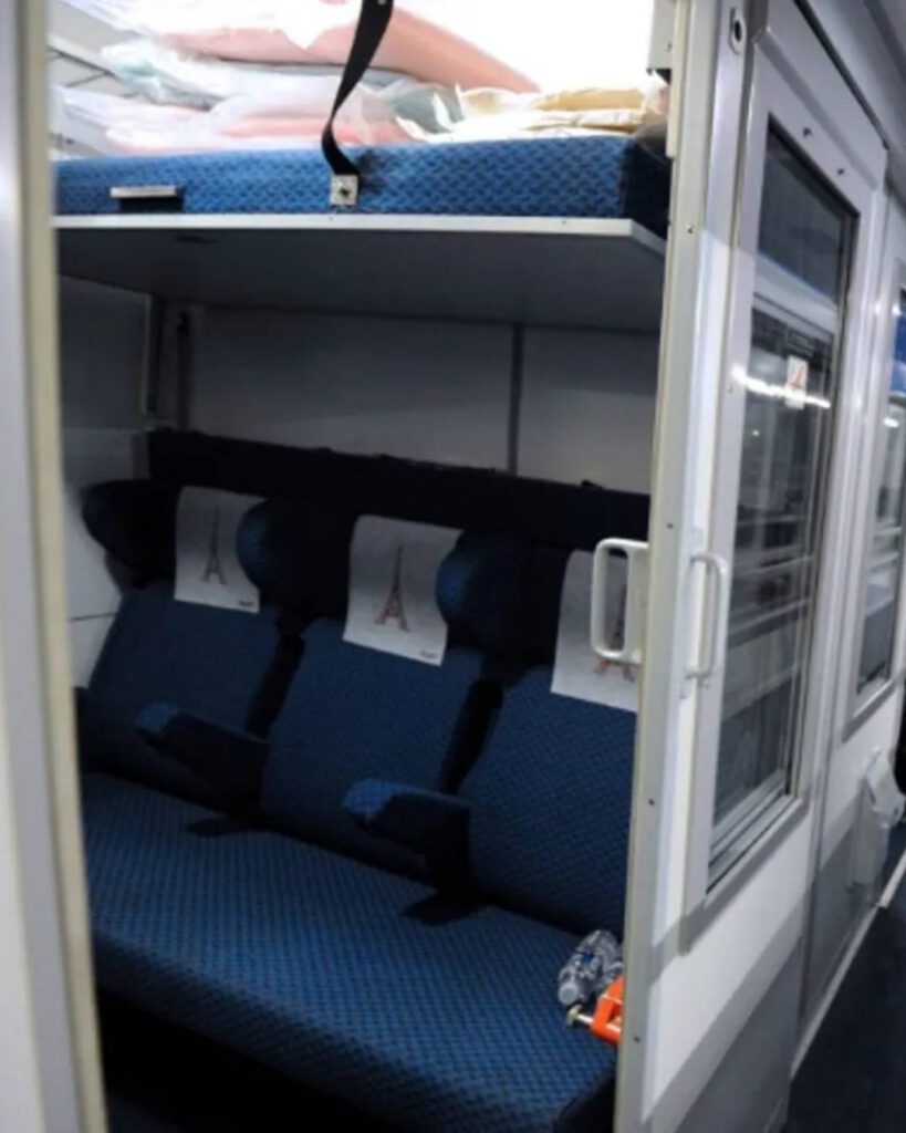 Compartiment couchettes d'un train de nuit : banquettes bleues, couchette relevée et fenêtre du couloir