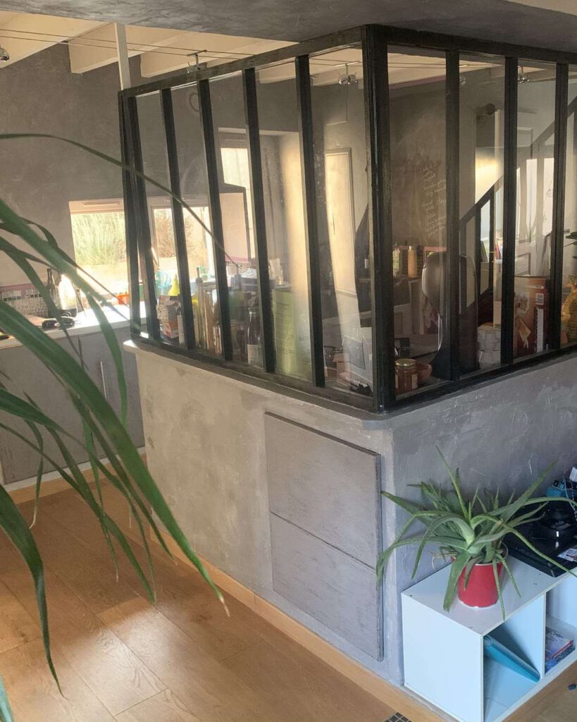 Intérieur d'une maison avec verrière atelier en acier séparant le séjour de la cuisine, plante en premier plan et parquet